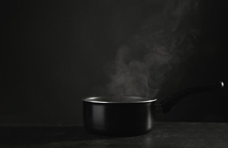 Saucepan with hot liquid on table against dark backgroundの写真素材