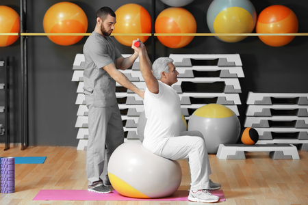 Rehabilitation concept. Mature man doing exercises under physiotherapist supervisionの写真素材