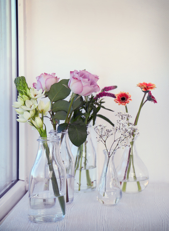Glass vases with beautiful bouquets of fresh flowers on windowsillの写真素材