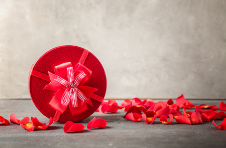 Gift box and rose petals on table