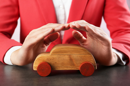 Car protection concept. Female hands and wooden toy car on tableの写真素材