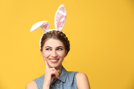 Beautiful young woman with bunny ears on color background