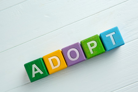Colorful cubes with word ADOPT on wooden background