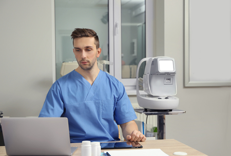 Handsome young ophthalmologist working in office