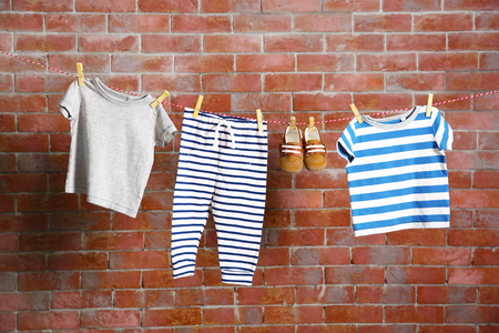 Clothesline with hanging baby clothes on dark brick-wall backgroundの写真素材