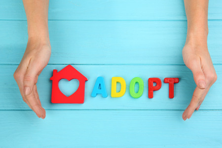 Female hands, word ADOPT and figure in shape of house on wooden backgroundの写真素材
