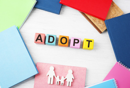 Colorful cubes with word ADOPT, figure in shape of family and notepads on wooden backgroundの写真素材