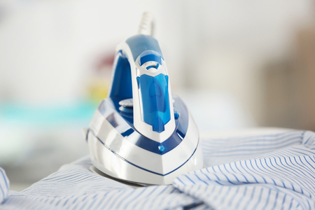 Electric iron and shirt on ironing board in roomの写真素材