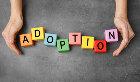 Female hands and colorful cubes with word ADOPTION on grey textured tableの写真素材