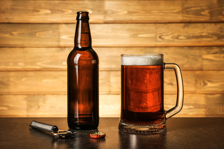 Mug of beer and bottle on table against wooden background