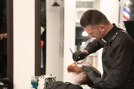 Hairdresser shaving client in barbershopの写真素材