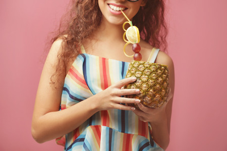 Young beautiful woman with cocktail in pineapple on color background