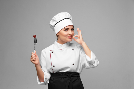 Portrait of young woman chef holding fork with grape on light backgroundの写真素材