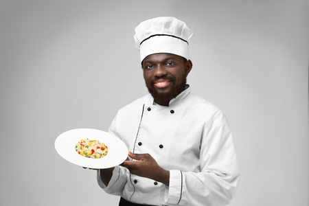 African American chef with plate of tasty salad on light backgroundの写真素材