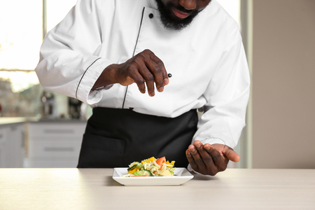 African American chef salting tasty salad in kitchenの写真素材