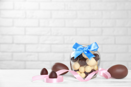 Glass jar with sweets and chocolate eggs on white tableの写真素材