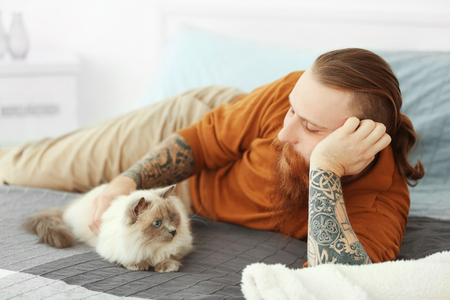 Young bearded man with fluffy cat lying on bedの写真素材