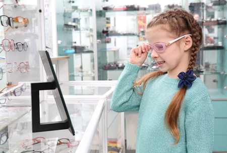 Cute little girl trying on new glasses in shopの写真素材