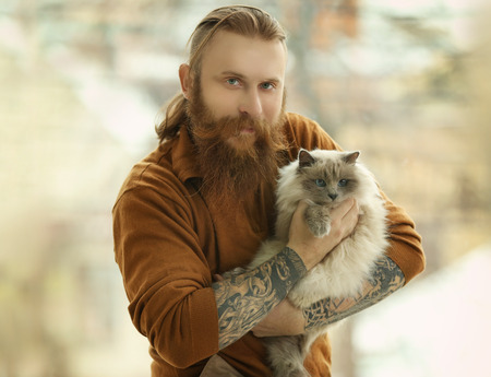 Young bearded man holding fluffy cat on blurred backgroundの写真素材