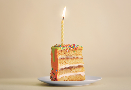Slice of birthday cake with candle on color backgroundの写真素材