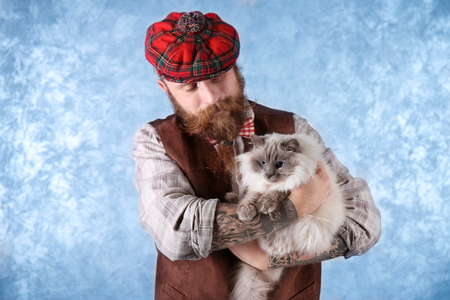 Young bearded man in plaid cap with fluffy cat on light backgroundの写真素材