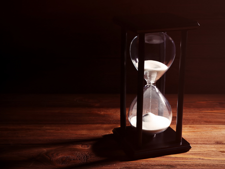 Time passing concept. Black hourglass with white sand on wooden background