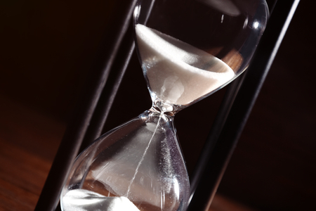 Time passing concept. Black hourglass with white sand on wooden background