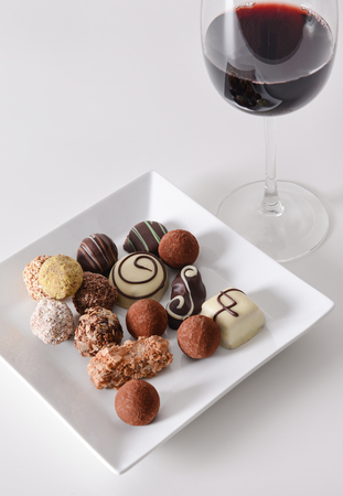 Delicious chocolate candies and red wine on white backgroundの写真素材