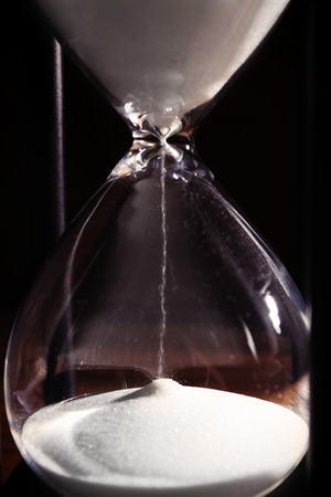 Time passing concept. Black hourglass with white sand, close up