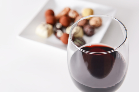 Glass of red wine and delicious chocolate candies on white backgroundの写真素材
