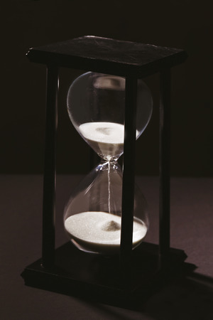 Time passing concept. Black hourglass with white sand on dark backgroundの写真素材