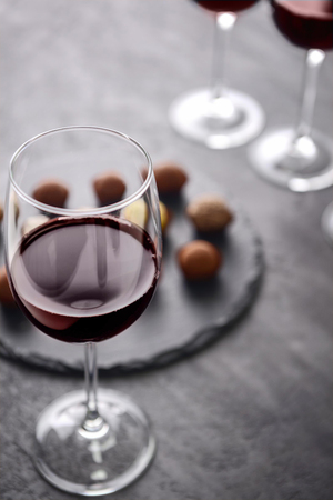 Glass of red wine and delicious chocolate truffles on grey backgroundの写真素材
