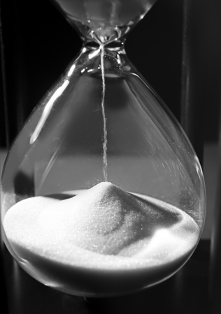 Time passing concept. Black hourglass with white sand on dark background
