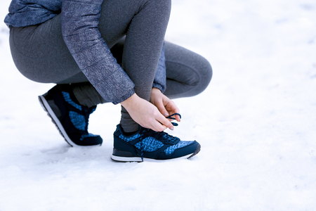 Young woman tying shoelaces in winter parkの写真素材