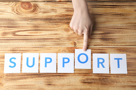 Female hand and word SUPPORT on wooden background