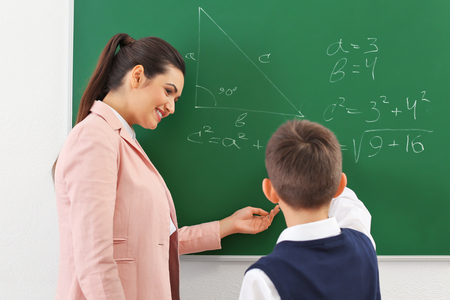 Teacher and schoolboy writing on blackboard in classroomの写真素材