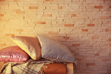 Three shiny decorative pillows on brick wall background