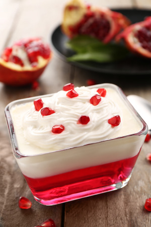 Tasty jelly dessert with pomegranate seeds and cream on wooden tableの写真素材