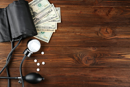 Pressure meter, pills and dollars on wooden background