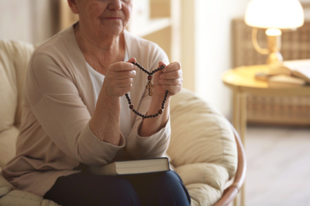 Elderly woman with Bible and rosary beads at homeの写真素材