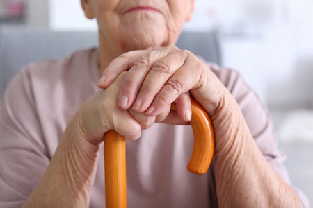 Elderly woman with walking stick at home, closeup