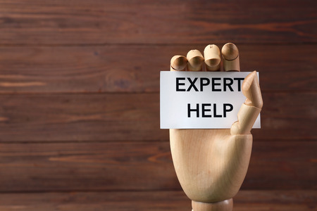 Mannequin hand holding white paper with phrase EXPERT HELP on wooden backgroundの写真素材