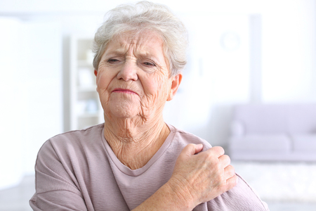 Elderly woman suffering from pain in shoulder at homeの写真素材