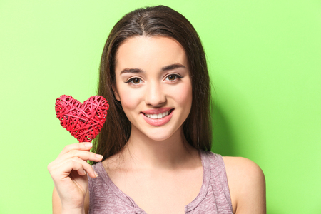 Beautiful young woman with decorative wicker heart on color backgroundの写真素材