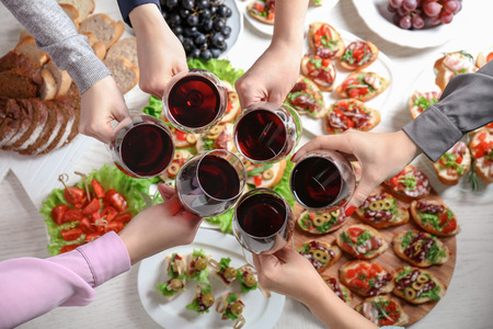 People clinking glasses with wine and delicious dishes on table