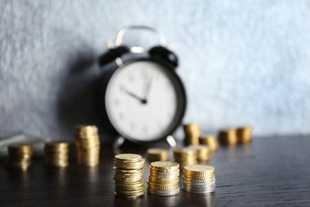 Money and alarm clock on wooden table