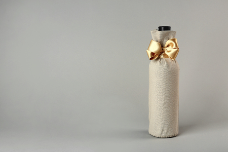 St. Valentine's Day concept. Wine bottle in gift linen pouch with satin ribbon on light backgroundの写真素材