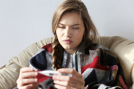 Young ill woman with electronic thermometer at home