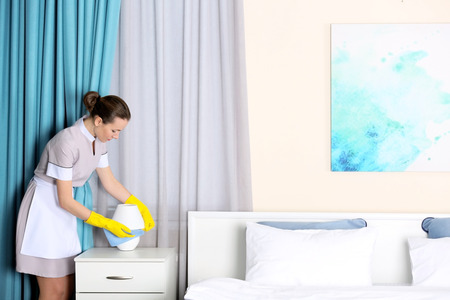 Hotel service concept. Chambermaid cleaning lamp on bedside table from dustの写真素材