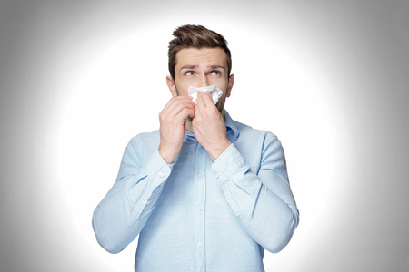 Young man using tissue to blow his nose on light backgroundの写真素材